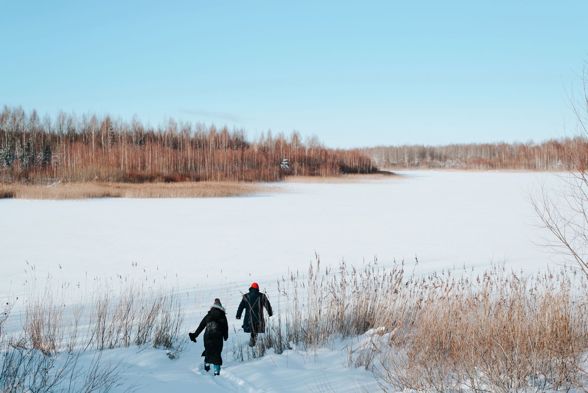 Two people run towards an open snowy field.