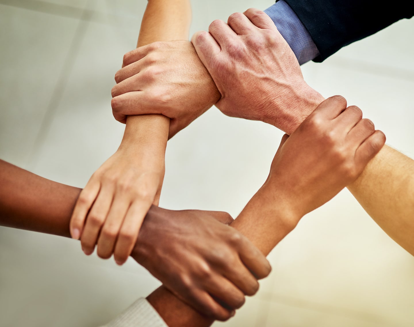 Close-up of several people linking arms by holding each other’s wrists. Symbolizes unity, teamwork, and mutual support.