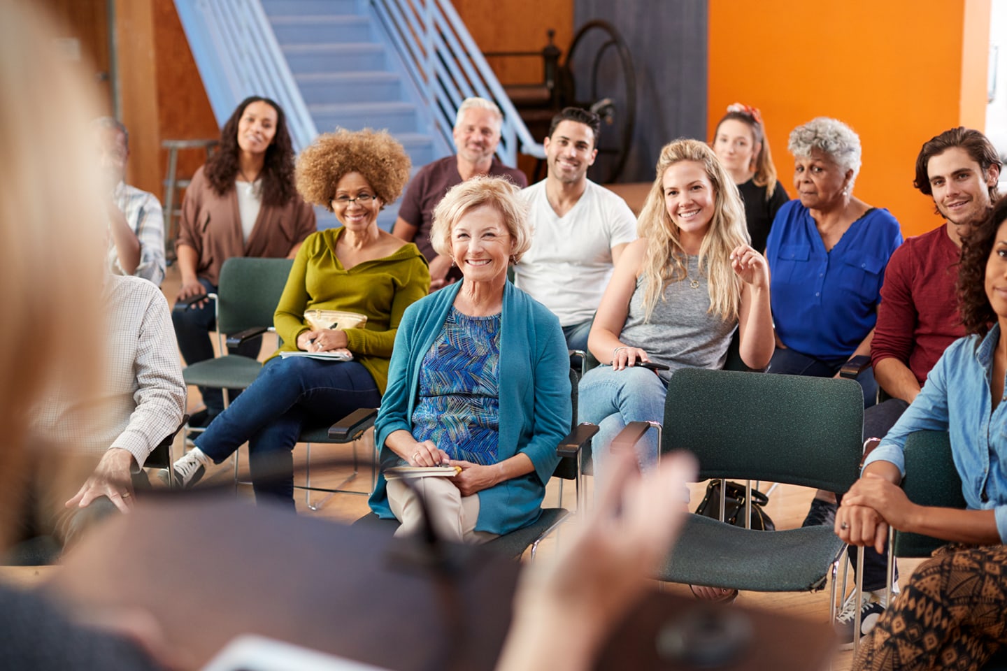 A diverse group of adults sit in a circle listening during a community meeting. Represents group discussion, support, and shared learning.