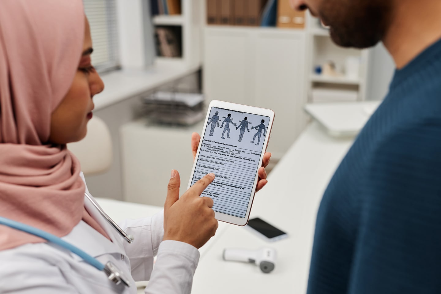 A doctor wearing a hijab shows medical information on a tablet to a patient, representing clear communication and shared understanding.